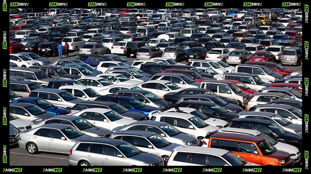 A large lot of imported used vehicles parked closely together at a Nigerian auto market.