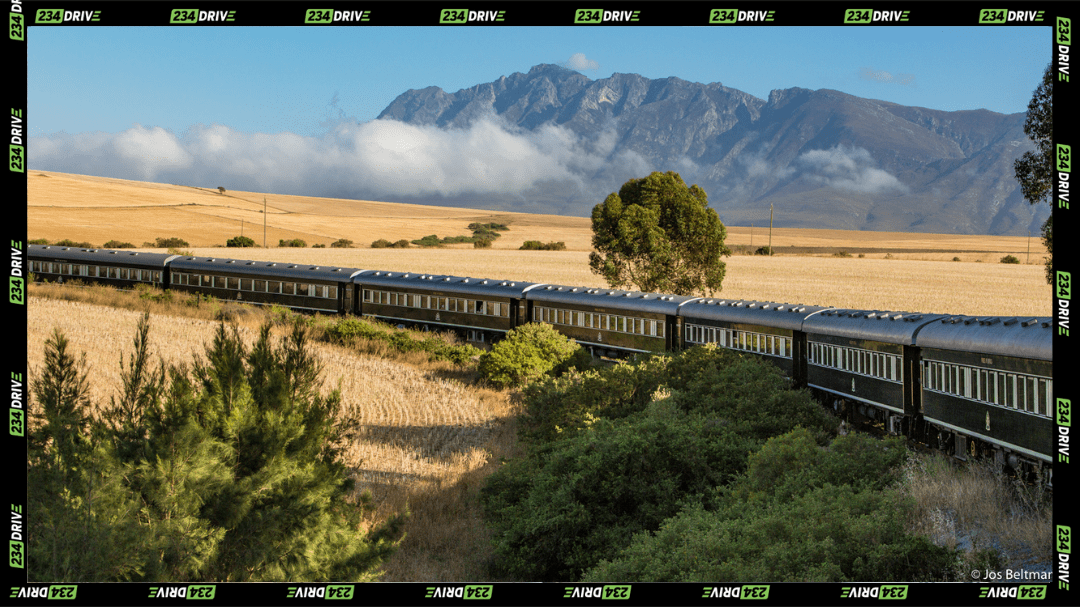 The Rovos Rail train moves quietly across open South African fields, carrying travellers through wide plains and mountain views. | Source: Rovos Rail