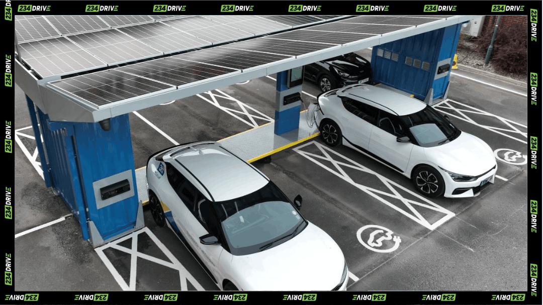 Two white electric cars charging under a solar panel canopy at a marked EV charging station.
