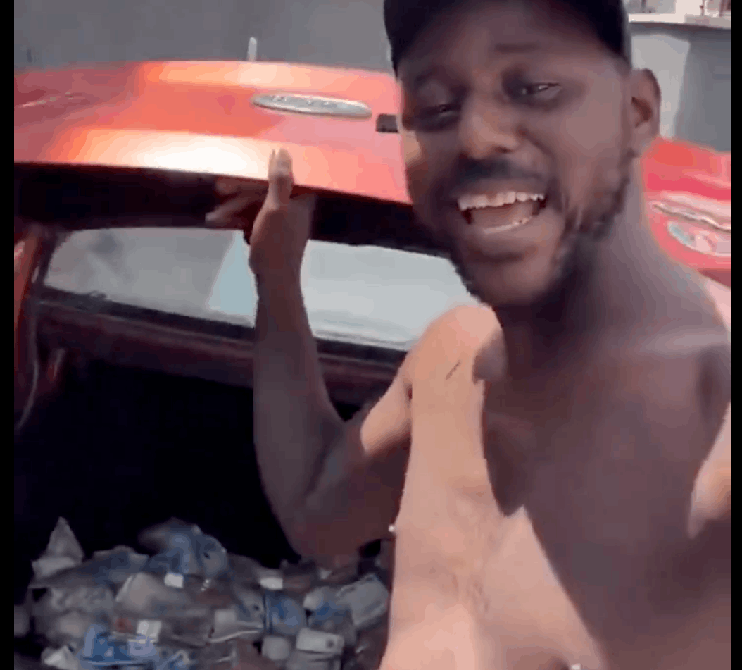Young man recording himself beside an orange vehicle shows how Lagos street begging can cross from roadside activity into social media content.