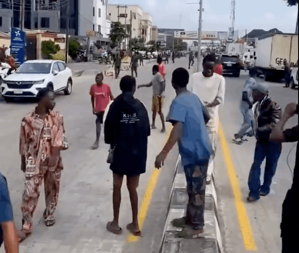 Young men gathered on and around a Lagos road divider illustrate the article’s focus on street begging, roadside pressure and public nuisance.