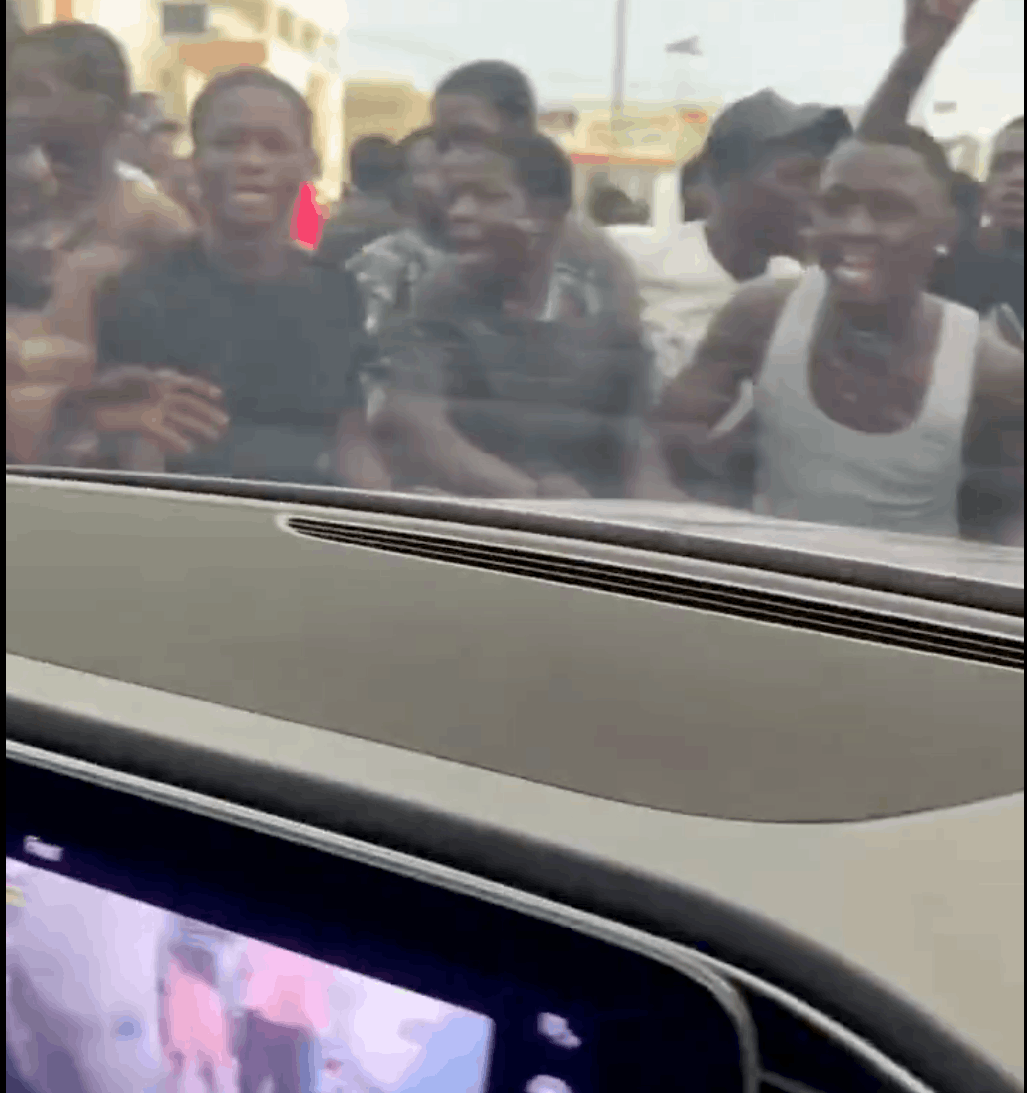 View from inside a car shows young men gathered at the window, illustrating Lagos street begging and pressure faced by motorists.