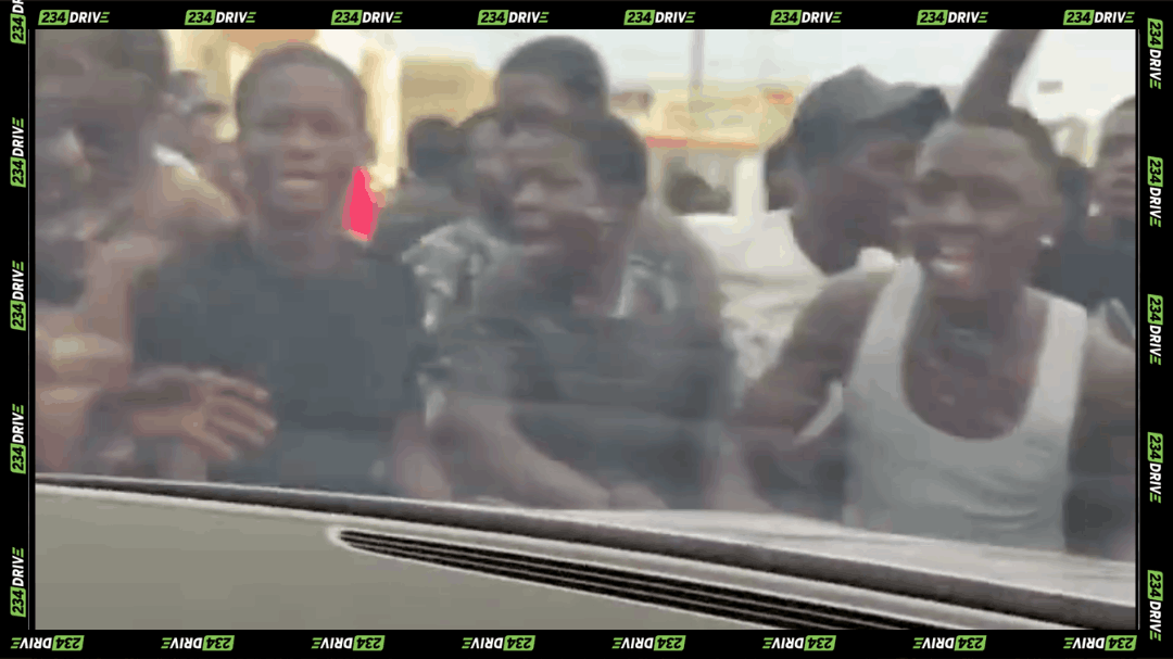 View from inside a car shows young men gathered at the window, illustrating Lagos street begging and pressure faced by motorists.