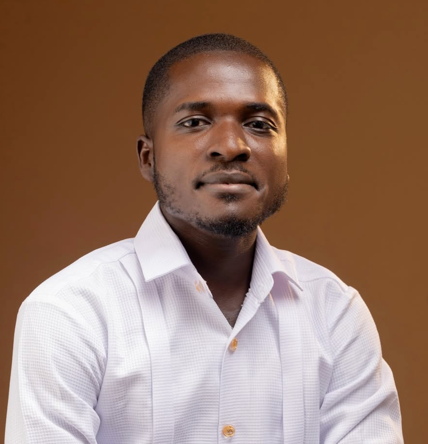 A man in a white shirt poses against a warm brown studio background for a profile exploring Mathias Charles Yabe and AkoFresh’s agromobility work.
