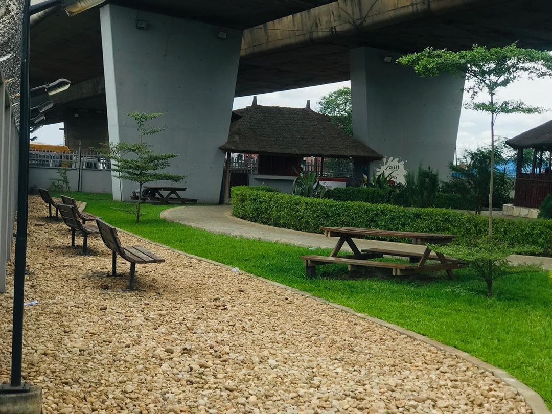 A landscaped public park with benches, lawns, and gravel pathways built underneath a flyover bridge in Lagos.