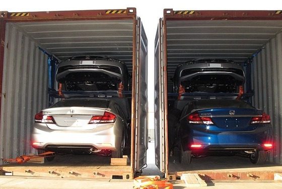 Two open shipping containers, each loaded with two Honda Civics, one stacked above the other on a car rack