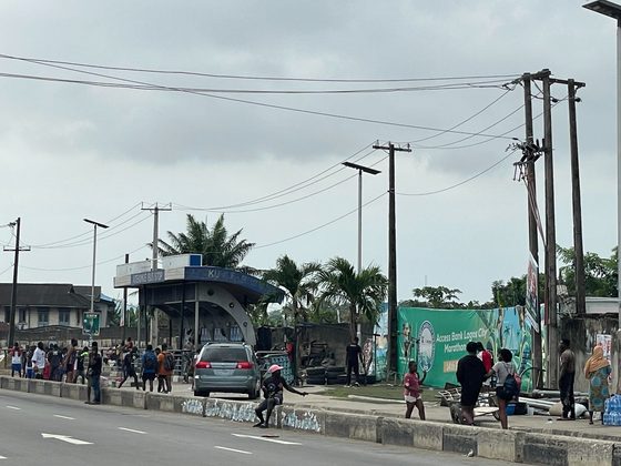 Lagosians working out and jogging along a major road shoulder near a bus stop and marathon banner in Lagos.