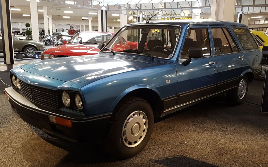 A vintage blue Peugeot 504 Break station wagon on display inside a motor show exhibition space