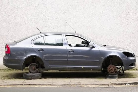 Grey saloon car parked on a kerb with its wheels and front headlight removed