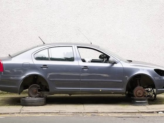 Grey saloon car parked on a kerb with its wheels and front headlight removed