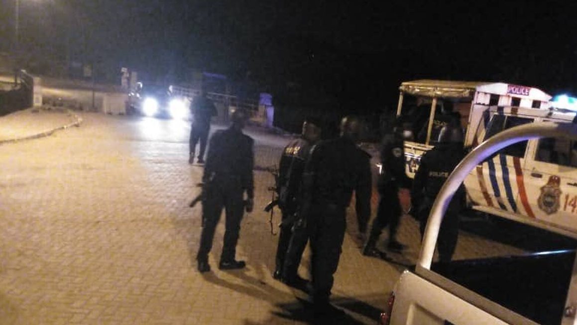 Armed Nigerian police officers standing beside a white patrol truck on a dark paved road at night