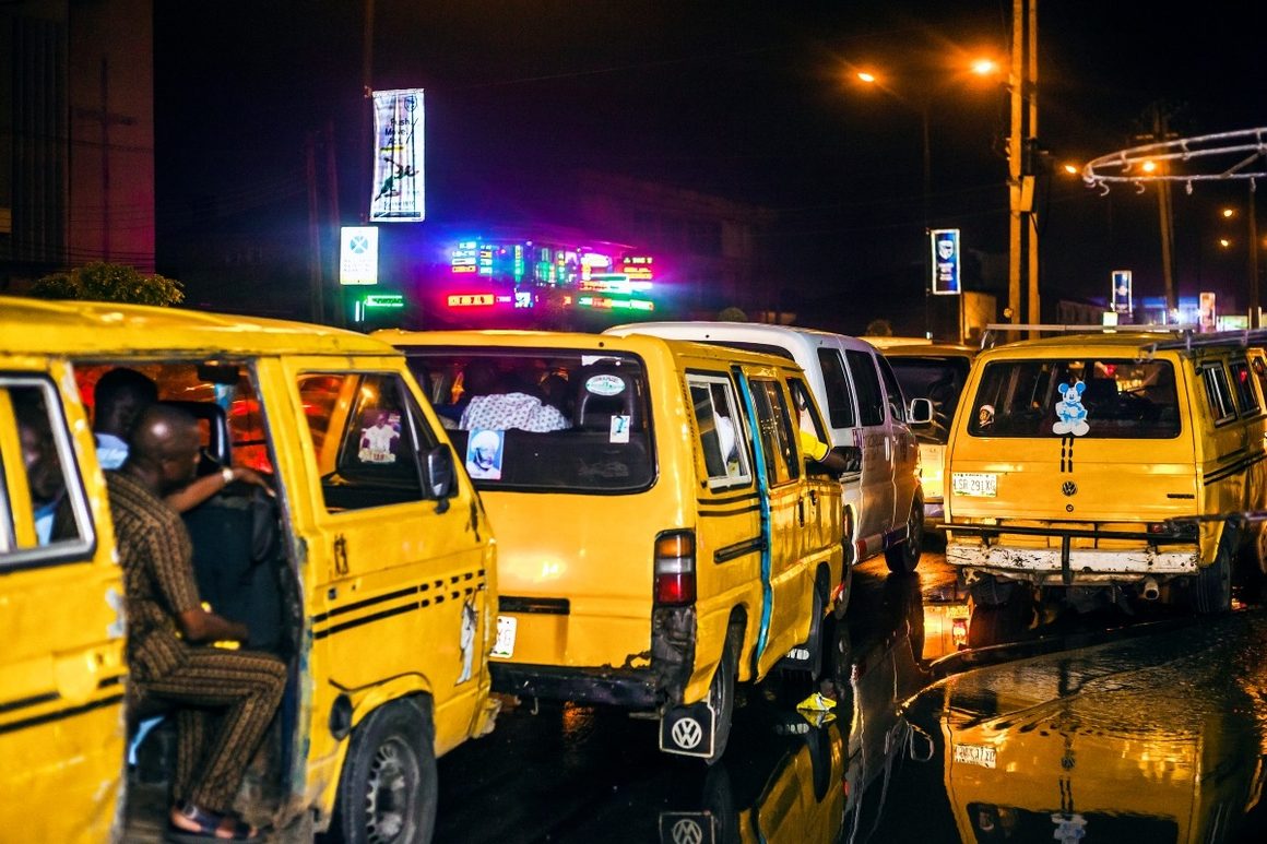 Close-up of yellow Danfo mini-buses packed together on a wet Lagos street at night with passengers inside
