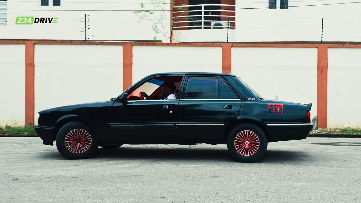 Side view of Ameen's black Peugeot 505 with red wheels beside a cream and orange wall